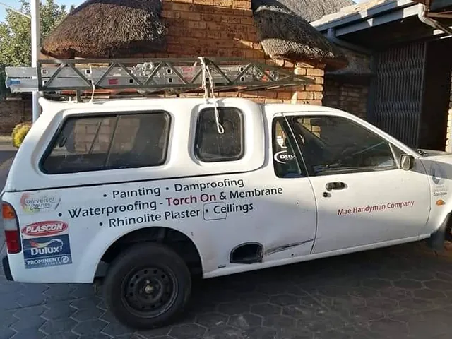 White Mae Handyman Company bakkie with ladders on the roof rack and its services lettered on the side