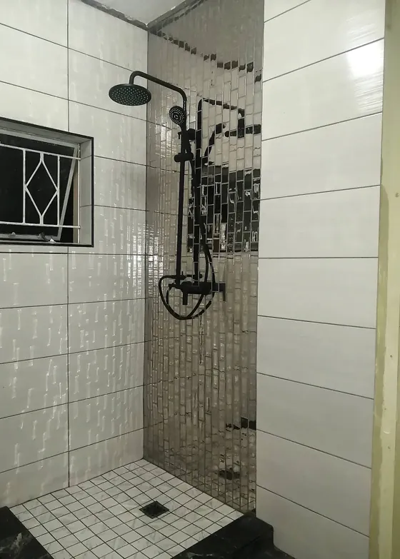 Finished shower with white wall tiles, a mirrored mosaic feature strip and black fittings